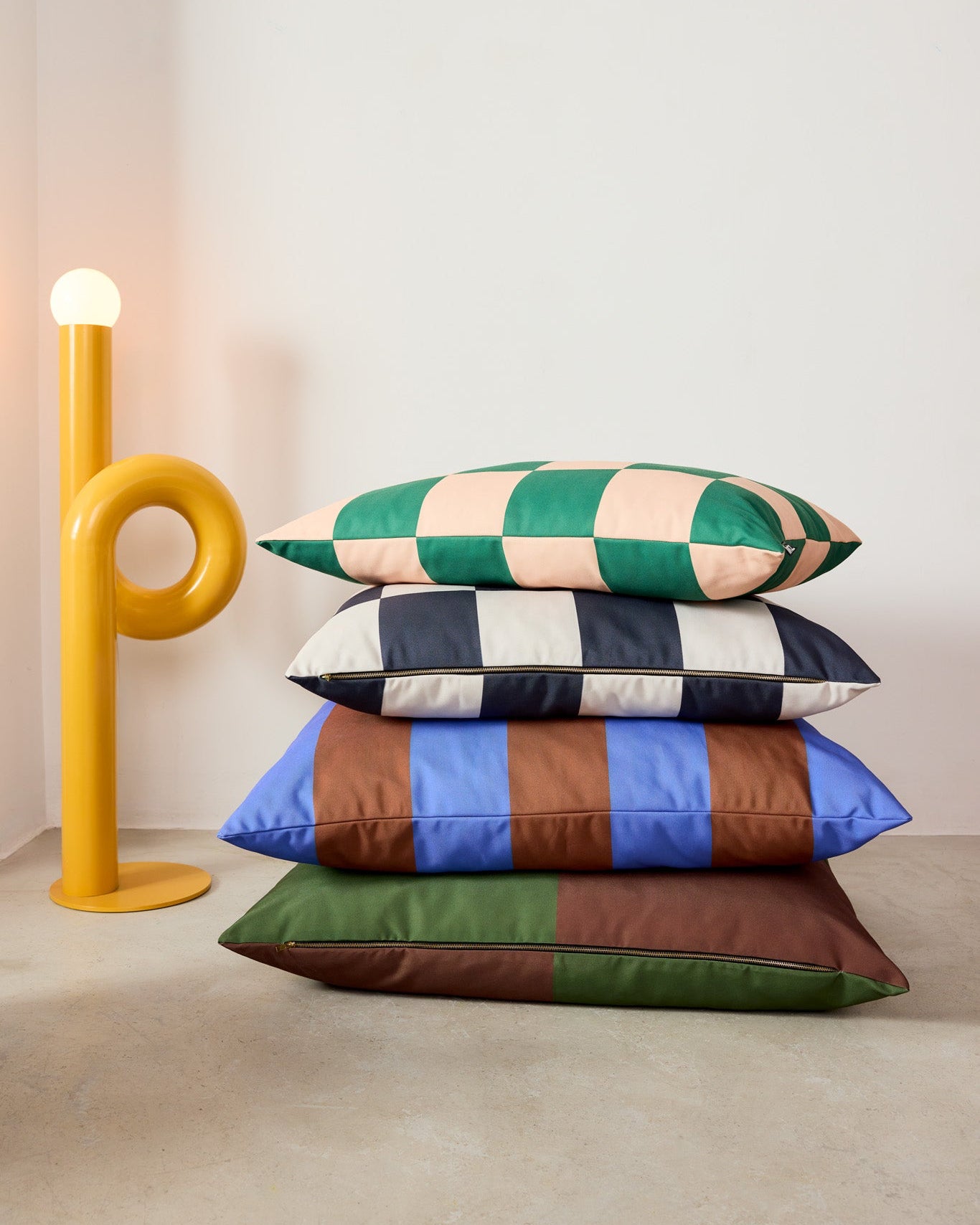 Stack of colorful striped dog pillows with a yellow lamp on a light background
