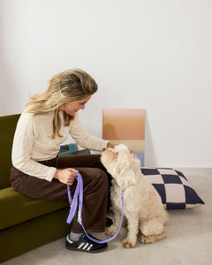 Woman sitting on a couch with a dog on a leash in a modern living room.