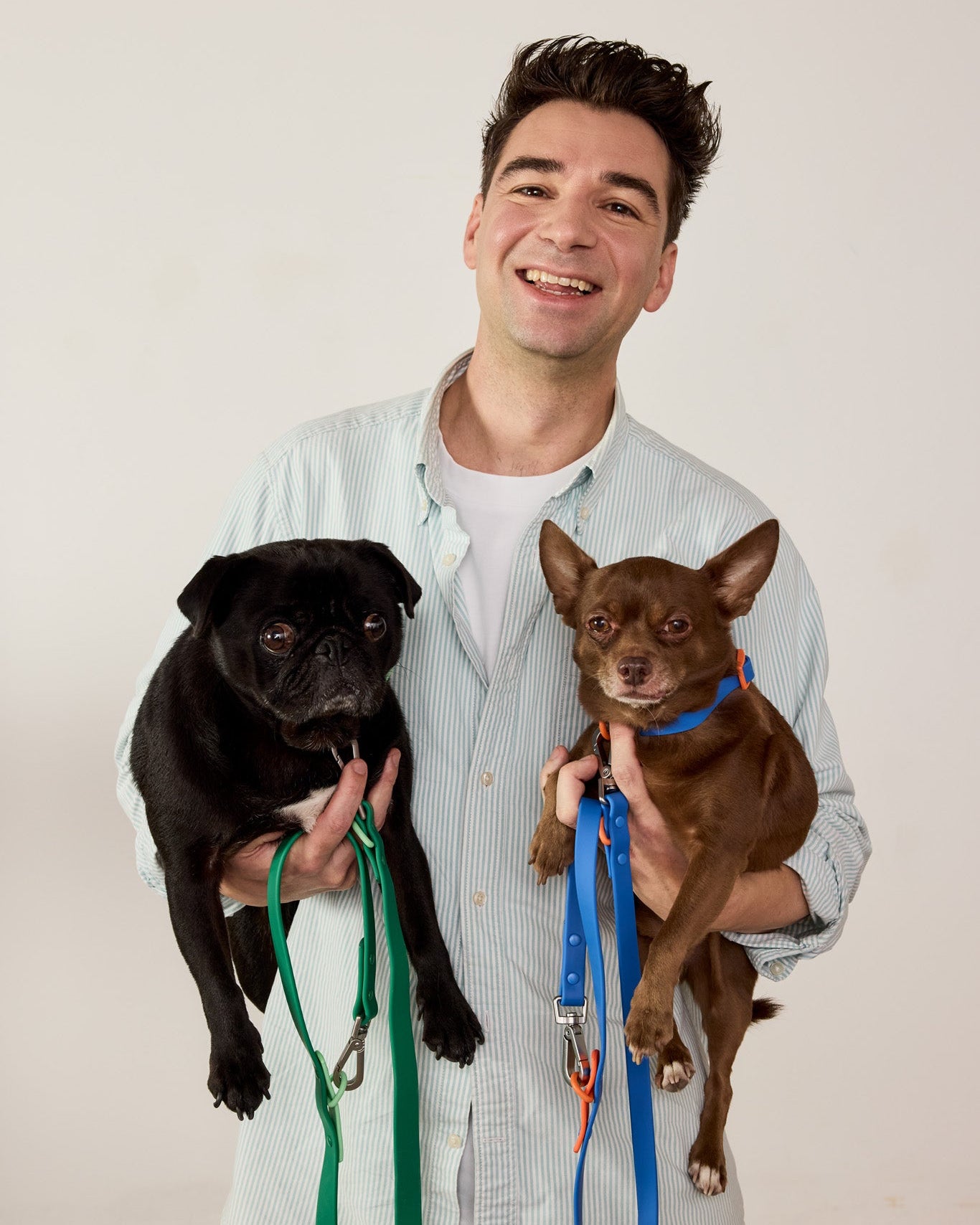 Man holding two dogs with leashes against a plain background